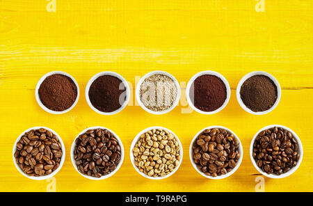 Assortiment de grains de café torréfié et de matières premières avec des motifs dans des bols en deux lignes sur un fond de bois jaune with copy space Banque D'Images