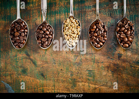 Frontière de l'assortiment de grains de café torréfiés dans vintage cuillères en argent sur un fond de bois rustique avec texture et copy space Banque D'Images