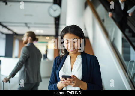 Smiling black lady texting message in airport Banque D'Images