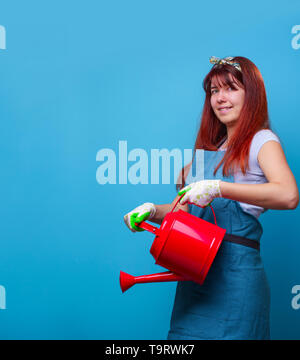 Photo de happy female florist avec un bidon vide dans ses mains sur fond bleu. Banque D'Images