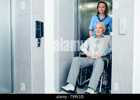 Infirmière réfléchie poussant senior patient in wheelchair at hospital ascenseur Banque D'Images