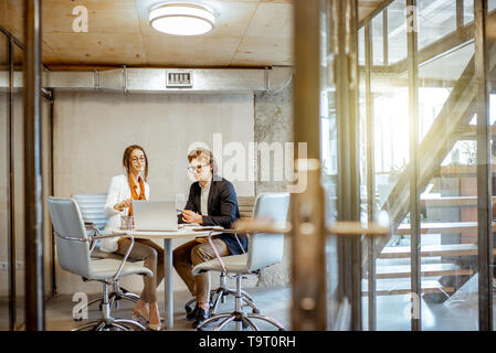 Jeune homme et femme ayant une conversation d'affaires au cours de la petite conférence, assis à la table ronde dans la salle de réunion