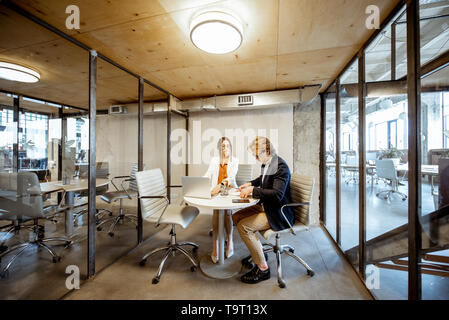 Homme et femme d'affaires travaillant dans la salle de réunion, une large vue sur l'intérieur de la pièce avec cloisons transparentes Banque D'Images