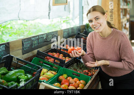 Souriante jeune femme choisissant les tomates en épicerie Banque D'Images