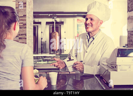 Homme mature cuisinier professionnel en uniforme en vue d'un client en cafe counter Banque D'Images