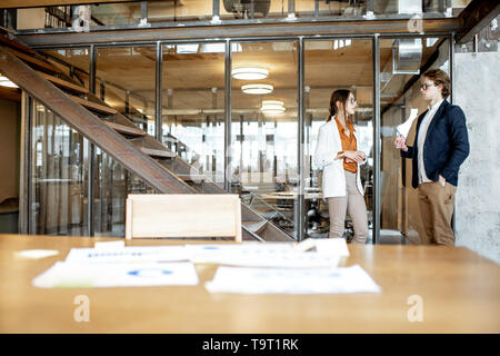 Les jeunes buiness man and woman ayant une conversation debout pendant la pause café dans le hall de l'office moderne, large vue de l'intérieur Banque D'Images