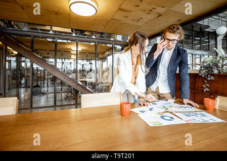 Jeune homme et femme d'affaires travaillant sur des documents à la table en bois au bureau ou espace de coworking Banque D'Images