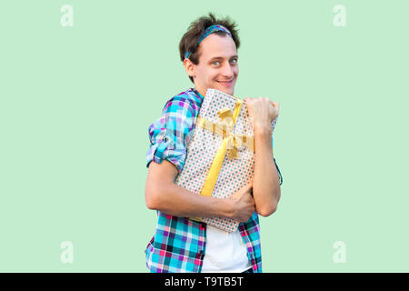 Portrait de plaisir jeune homme en blanc taille basse t-shirt et chemise à carreaux et s'étreindre permanent présent avec bow jaune, sourire malicieux, looking at camera Banque D'Images