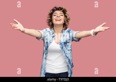 Donne-moi dans ses bras. Portrait de jeune femme avec les cheveux bouclés casual shirt bleu debout avec les bras levés pour embrasser et looking at camera, smi dentelée Banque D'Images