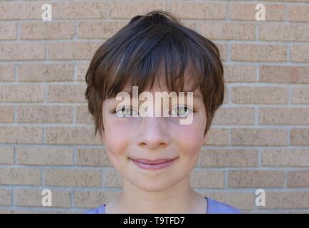 Visage de jeune enfant avec de superbes yeux noisette, cheveux bruns courts et ses fossettes Pixie Banque D'Images