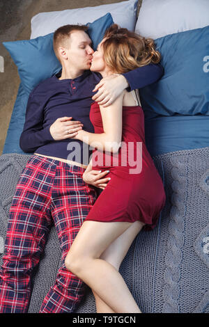 Portrait de joli jeune famille se reposer dans la chambre à coucher, en vêtements de lying on bed with blue plaid s'embrassent. Femme avec l'amour de toucher sa Banque D'Images