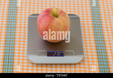 Une pomme rouge est sur une balance électronique sur la table à l'intérieur. Banque D'Images