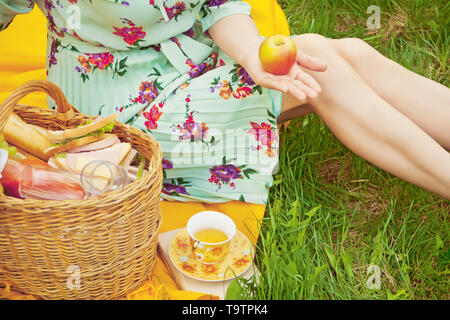 Femme sur le pique-nique se trouve sur la couverture jaune et est titulaire d'Apple. Près de panier avec de la nourriture, des fruits et une tasse de thé. Banque D'Images