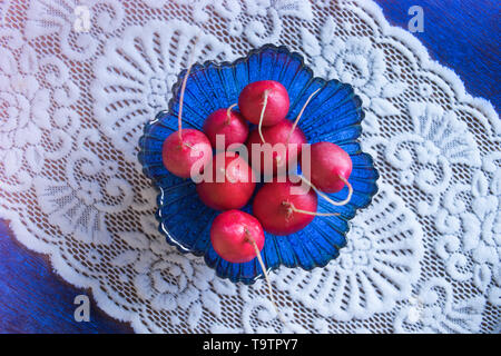 Les radis frais mûrs dans un saladier en verre bleu. Table avec nappe blanche magnifique. Banque D'Images