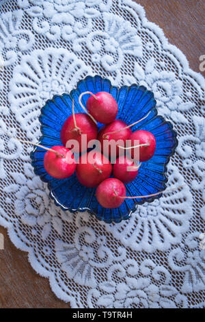 Les radis frais mûrs dans un saladier en verre bleu sur une table en bois avec une belle nappe blanche. Vue d'en haut Banque D'Images