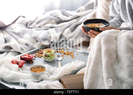 Femme avec de délicieuses barres granola et yogourt dans un bol sitting on bed Banque D'Images