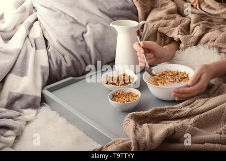 Woman eating tasty barres granola avec yogourt on bed Banque D'Images