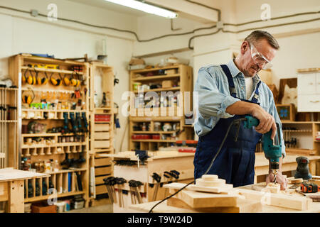 Taille portrait of senior carpenter percer le bois tout en travaillant en menuiserie, copy space Banque D'Images