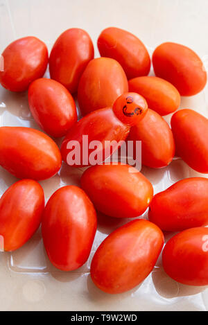 Tomate de forme impaire dans une caillebotis de tomates avec la face dessinée ajoutée. Fruits et légumes humoristiques ressemblant au personnage de M. Blobby Banque D'Images