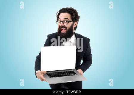 L'homme en blanc avec écran, cheerful young bearded man holding laptop sur fond bleu Banque D'Images