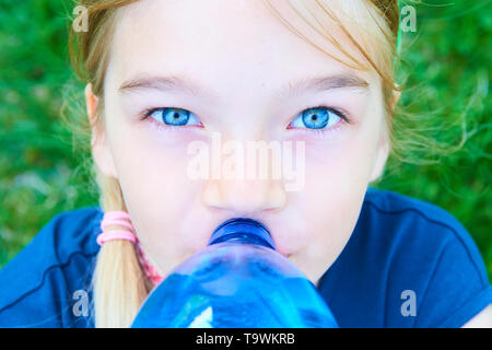 Close up portrait of girl adorable aux yeux bleus l'eau potable de la bouteille bleue en plastique avec fond de verdure Banque D'Images