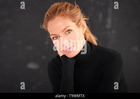 Portrait de femme portant un magnifique col roulé rouleau et looking at camera while sitting with hand on chin à fond sombre. Banque D'Images