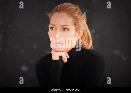 Close-up portrait de belle blonde mature woman sitting at fond sombre alors que la rêverie. Banque D'Images