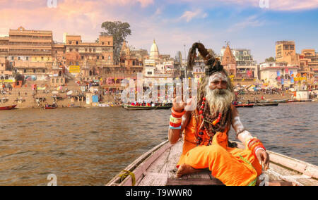 Sadhu baba assis sur un bateau en bois avec vue sur l'architecture historique de la ville de Varanasi avec Gange ghat au coucher du soleil. Banque D'Images