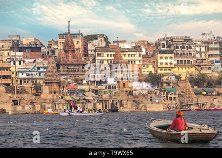 L'homme âgé assis sur un bateau en bois sur le fleuve Ganges Varanasi Inde historique surplombant la ville architecture au coucher du soleil Banque D'Images