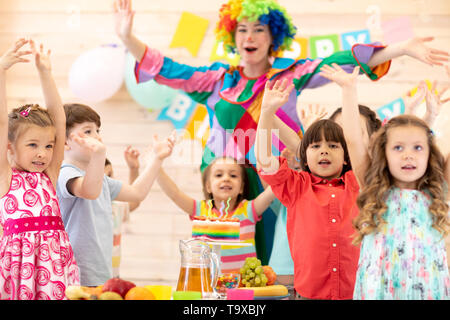 Clown jouant avec des enfants. Groupe enfants célébrer anniversaire et posent pour la caméra debout avec les mains jusqu'à la table. Maison de vacances dans un club pour enfants. Banque D'Images