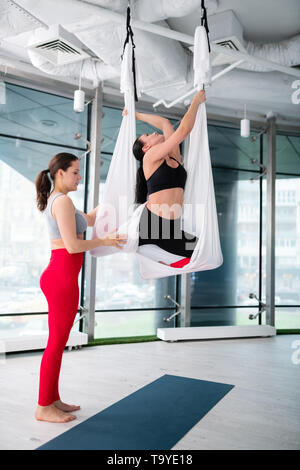 Dark-haired yoga trainer helping son étudiante d'essayer le yoga aérien Banque D'Images