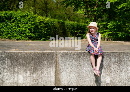 Portrait of cute smiling girl wearing hat assis sur mur de retenue Banque D'Images