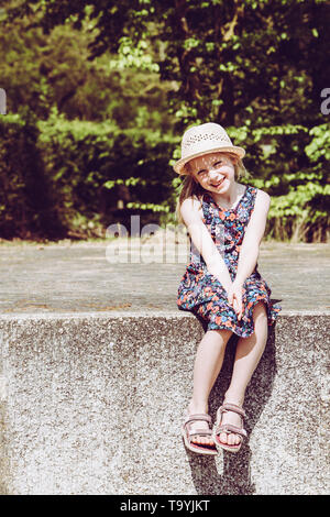 Portrait of cute smiling girl wearing hat assis sur mur de retenue Banque D'Images