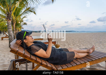 L'utilisation touristique asiatique tablette pour surfer sur Internet sur la plage Banque D'Images