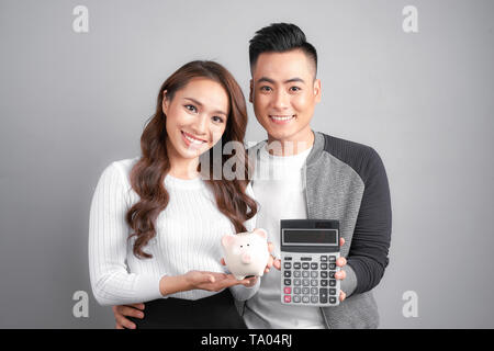 Jeune couple tenir cochon rose bank et calculatrice isolé sur fond gris Banque D'Images