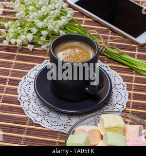 Tasse de café noir avec du lait sur une soucoupe, guimauves, un bouquet de lys de la vallée et un smartphone sur la table Banque D'Images