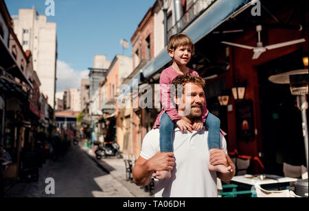 Père avec petite fille debout à l'extérieur sur rue dans la ville méditerranéenne, donnant un piggyback ride. Banque D'Images