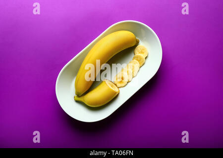 Plaque avec de délicieuses bananes coupées sur un fond de couleur Banque D'Images