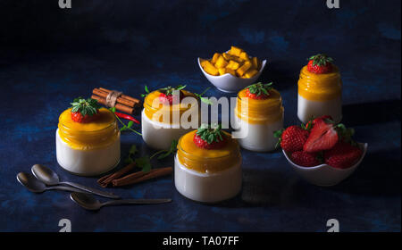 Dessert sucré traditionnel italien panna cotta à la mangue gelée avec Touch of red hot chili Piri-Piri servis dans des bocaux sur table en bois blanc et embellis Banque D'Images