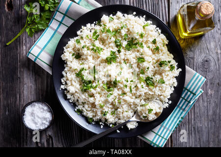 Vue de dessus le chou-fleur du riz ou du couscous mélangé avec de persil finement haché dans un bol noir sur une vieille table rustique, vue horizontale à partir de ci-dessus, cl Banque D'Images