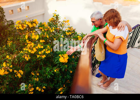Senior couple admiring blooming fleurs jaunes en jardin de l'hôtel. Les personnes bénéficiant des vacances d'été. Concept de voyage Banque D'Images