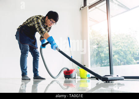 Jeune homme séduisant est vide de nettoyage Le nettoyage de l'équipement commercial sur le plancher à la maison aider femme Banque D'Images