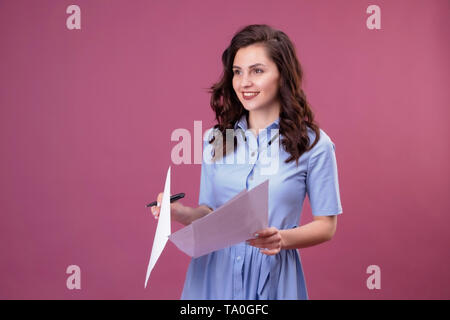 Jeune femme avec des points d'un de feuilles de papier, est titulaire d'un stylo. Élève de se préparer pour l'examen sur fond rose Banque D'Images