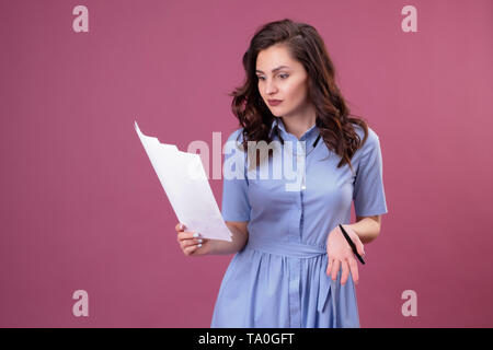 Jeune femme avec des points d'un de feuilles de papier, est titulaire d'un stylo. Élève de se préparer pour l'examen sur fond rose Banque D'Images