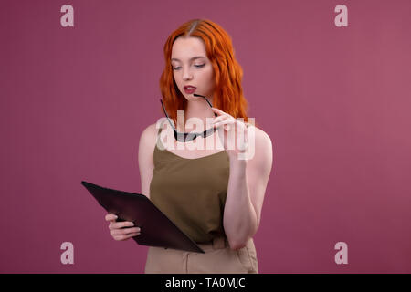 Portrait d'une femme rousse avec des lunettes et des dossiers des élèves. l'université ou au collège sur fond rose Banque D'Images