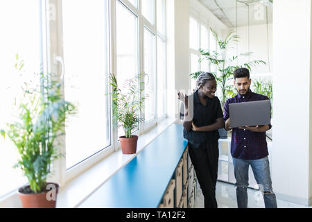 Businessman and businesswoman using a laptop together while standing in front of office building fenêtres donnant sur la ville Banque D'Images