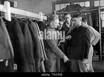 Après la fin de la guerre civile espagnole (avril 1939), les soldats de la Wehrmacht de la légion Condor ont reçu des vêtements civils par leurs camarades à leur retour en Allemagne en mai 1939. Un soldat est le réglage d'une veste pour un camarade. Derrière, il y a d'autres soldats debout. Sur la gauche, vestes et manteaux suspendu à la tringle. Banque D'Images