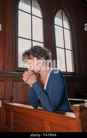 Jeune femme qui prie dans l'église avec les mains pliées Banque D'Images