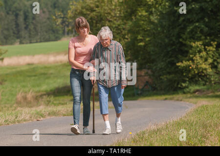 Jeune femme aider senior woman walking with stick Banque D'Images