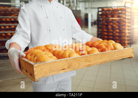 Baker's mains tiennent un plateau avec du pain frais à la boulangerie. Concept de boulangerie. Banque D'Images